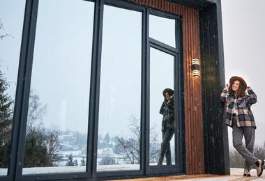 A woman standing on a winter terrace near bifold patio doors connecting an indoor living space with an outdoor patio during cold weather.