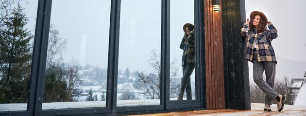 A woman standing on a winter terrace near bifold patio doors connecting an indoor living space with an outdoor patio during cold weather.