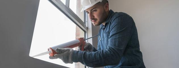Professional contractor applying exterior caulk around a residential window frame