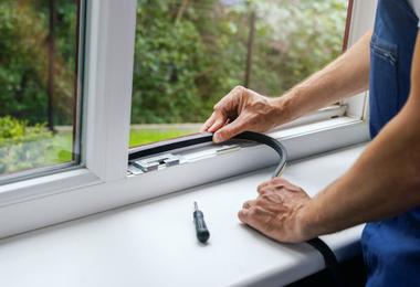 Worker installing sealing tape on a plastic window frame to prevent air and moisture leaks