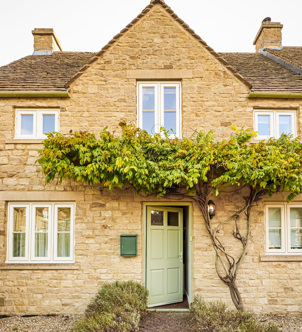 Cotswold cottage with classic casement windows, pastel frames, and small-pane grilles set into honey-coloured limestone walls.