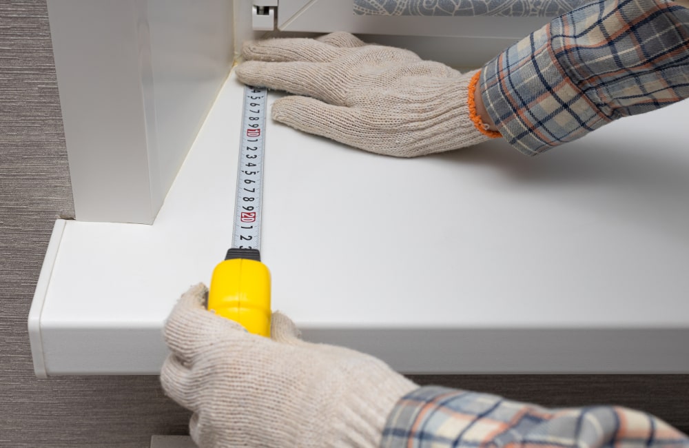 Homeowner measuring an exterior window sill to assess damage and plan proper replacement