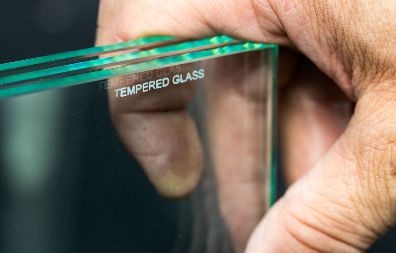 Glazier holding a finished glass pane in an industrial setting, illustrating window glass processing and durability.
