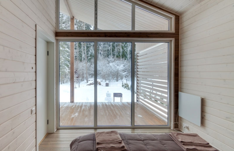 Cozy bedroom interior with large glass bifold patio doors offering a winter forest view.