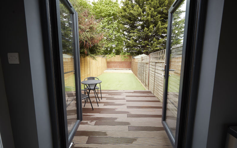 Backyard garden visible through open bifold patio doors, highlighting seamless indoor-outdoor flow and large opening potential.