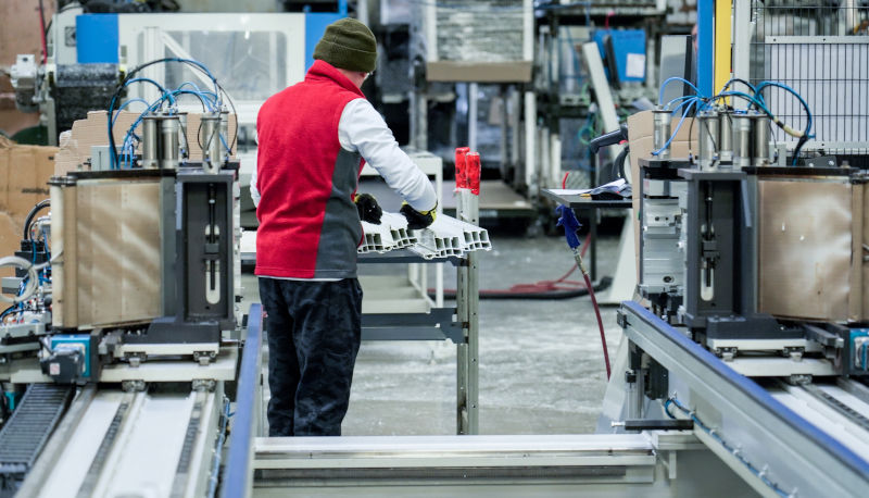 Worker assembling vinyl window frames in a factory, showing the manufacturing process and production stage