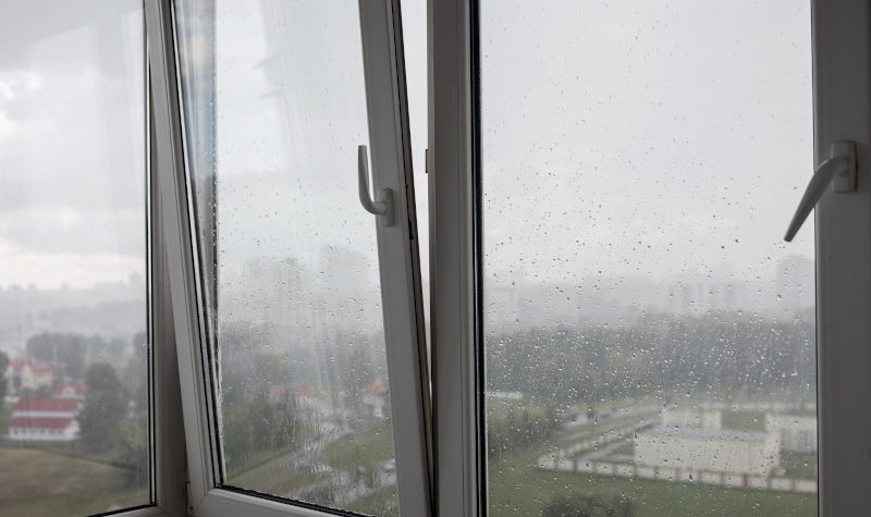 Rain droplets on balcony glass windows illustrating moisture exposure and potential window seal stress