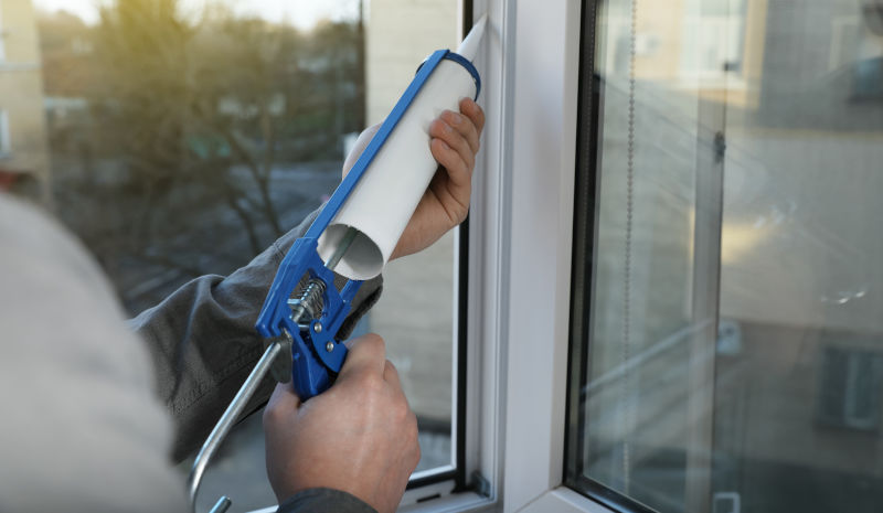Applying silicone caulk around a window frame during a home maintenance project